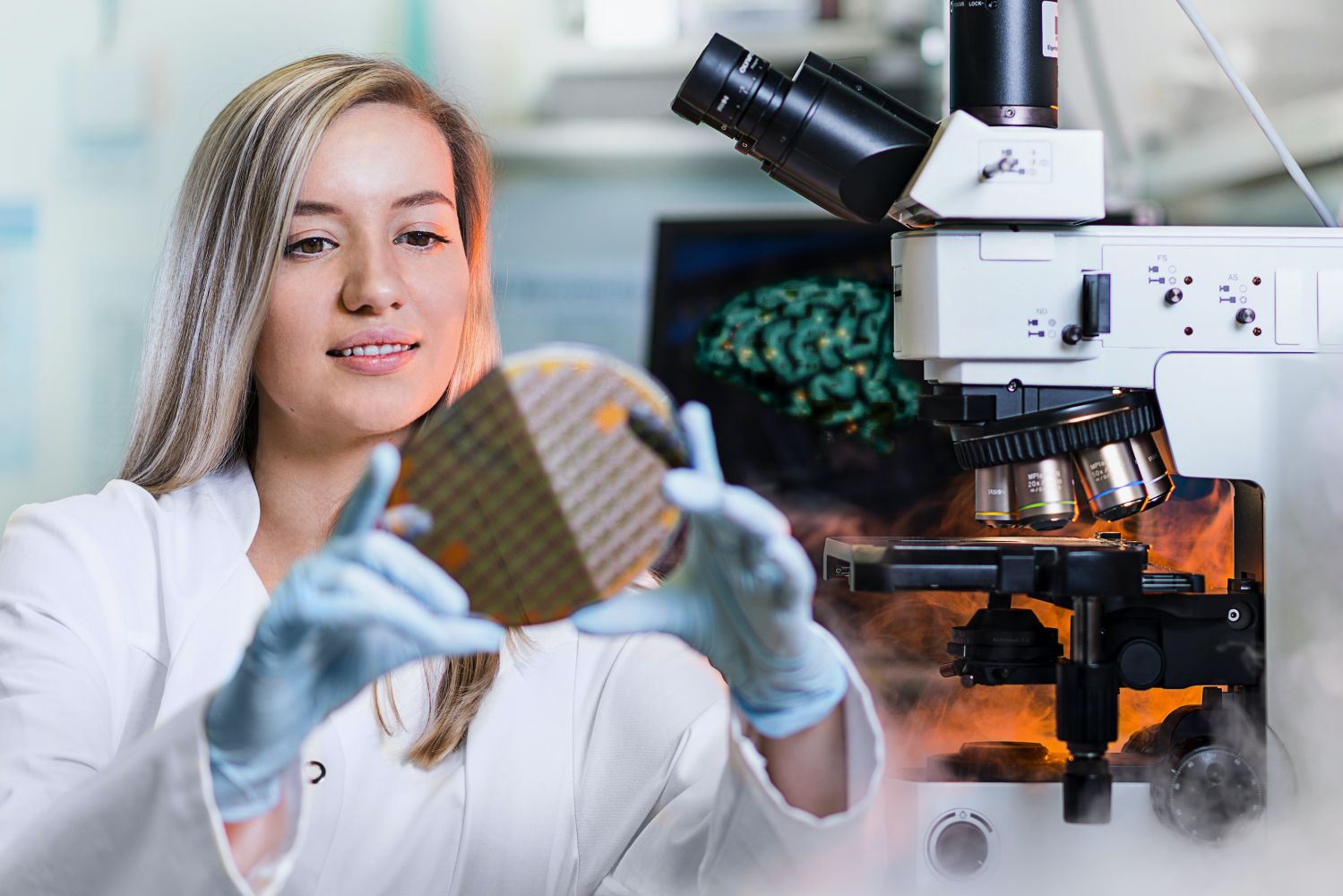 Frau hält Wafer in den Händen, im Hintergrund Labortechnik